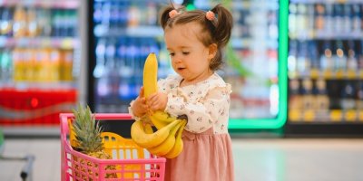 Malá holčička s dětským nákupním vozíkem v supermarketu nakupuje ovoce