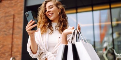 Mladá žena s nákupními taškami se dívá do telefonu