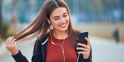Usmívající se mladá žena s drátovými sluchátky a mobilním telefonem