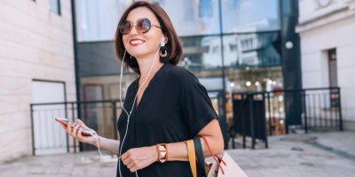Usmívající se žena s drátovými sluchátky a mobilním telefonem v městském prostředí