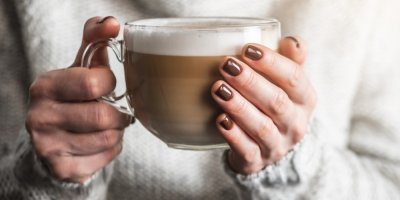 Žena s hnědě nalakovanými nehty drží šálek latte