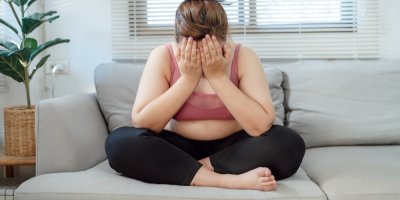 Žena s nadváhou sedí na pohovce s hlavou v dlaních