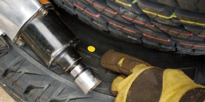 Ruka v pracovní rukavici ukazující na žlutou tečku na pneumatice