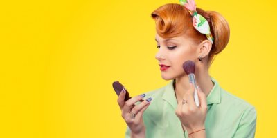 Mladá žena v retro účesu si upravuje make-up před zrcátkem