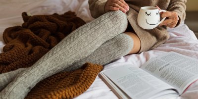 Žena s šálkem čaje si čte v posteli knihu.