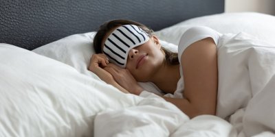 Žena spí v posteli s pruhovanou maskou na očích