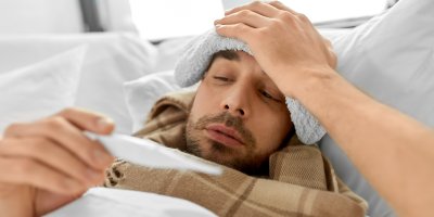 Nemocný muž s obkladem na hlavě si prohlíží teploměr