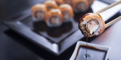 Sklenice se sójovou omáčkou vedle talíře se sushi