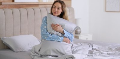 Žena v pyžamu sedí v posteli a objímá hedvábný polštář