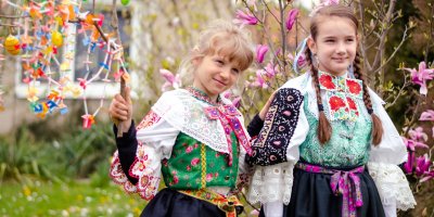 Dvě dívky v krojích, jedna drží větev s velikonočními dekoracemi
