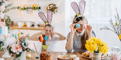 Žena a dívka mají na hlavě čelenky s králičíma ušima a připravují jarní dekorace z vajíček