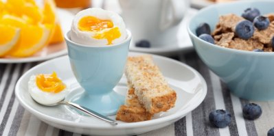 Vejce naměkko v modrém kalíšku na snídani, kousky toustu, borůvky, cereálie
