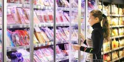 Žena v supermarketu se dívá do regálu s šunkami