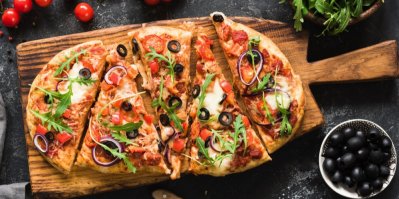 Pizza s rukolou a černými olivami na dřevěném prkénku