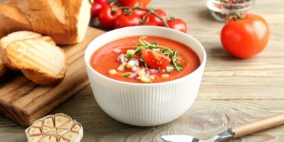 Studená polévka gazpacho v bílé misce, rajčata, bageta a česnek