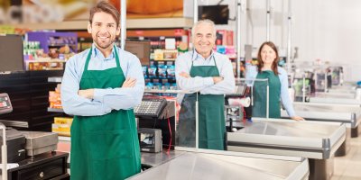 Prodavači v zeleném stejnokroji stojící u pokladen v supermarketu 