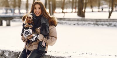 Dívka drží v náručí psa v zimním oblečku 