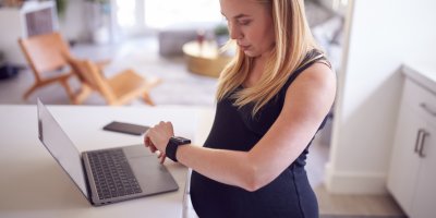 Těhotná žena se u notebooku dívá na své chytré hodinky