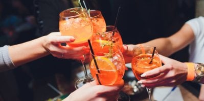 Několik žen si přiťukává skleničkami s namíchaným drinkem Aperol Spritz s pomerančem