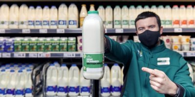 Prodavač v supermarketu podává láhev s mlékem