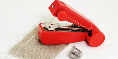 Malý červený příruční šicí stroj, látka, náprstek