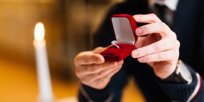 Muž drží v ruce otevřenou krabičku se zásnubním prstenem