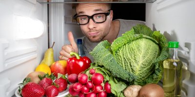 Muž s brýlemi se dívá do lednice, ve které je olej, ovoce a zelenina