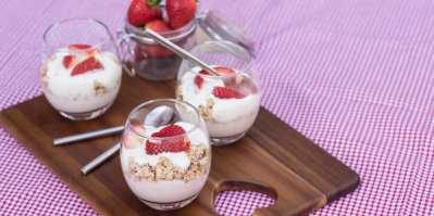 Servírování bílého jogurtu ve sklenici s müsli a jahodami