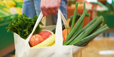 Ruka drží plátěnou tašku s ovocem a zeleninou