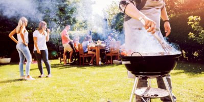 Gril s masem, v pozadí sedí lidé u zahradního stolu