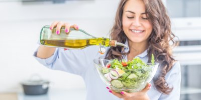 Žena zalévá mísu zeleninového salátu olivovým olejem