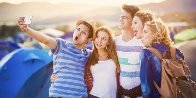 Skupina přátel si fotí selfie před stany na festivalu