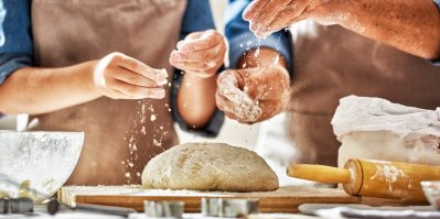 Muž a žena sypou mouku na domácí chléb