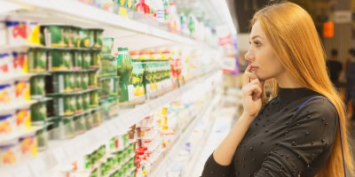 Žena si vybírá jogurt z regálu mléčných výrobků v supermarketu