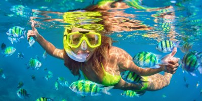 Dívka potápějící se se šnorchlem a maskou mezi exotickými, mořskými rybami
