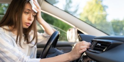Zpocená žena v autě nastavuje klimatizaci