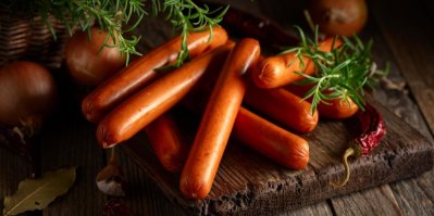 Párky na dřevěném prkénku, vedle rozmarýn, cibule a chilli paprička