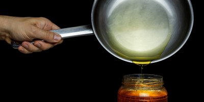 Slévání oleje z pánve do skleněné nádoby
