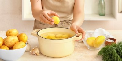 Žena vložila do hrnce oškrábané brambory a chystá se je uvařit