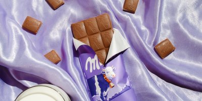Rozbalená a nalámaná čokoláda Milka na fialovém podkladu