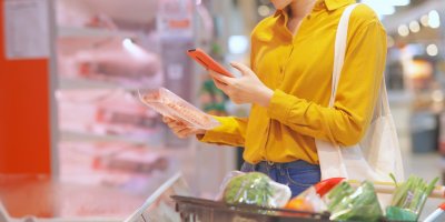 Žena v supermarketu skenuje balíček šunky pomocí mobilního telefonu
