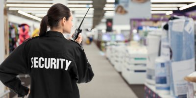 Žena s bundou s nápisem „security“ a vysílačkou v supermarketu
