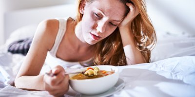 Žena s bolestí hlavy jí polévku v posteli