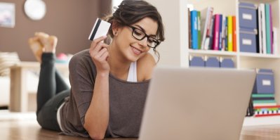 Žena leží před počítačem a drží platební kartu
