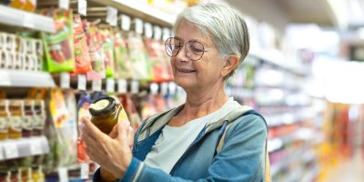 Starší žena si prohlíží sklenici okurek v obchodě