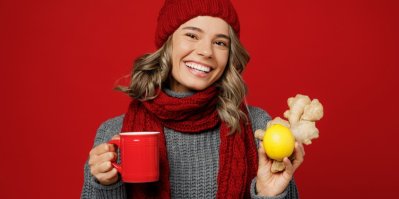 Žena v čepici a šále drží zázvor, citron a hrnek