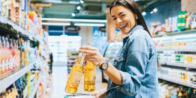 Mrkající žena s nákupním vozíkem drží v supermarketu dvě lahve alkoholu