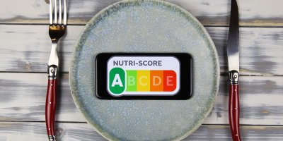 Talíř, na němž leží mobilní telefon, na kterém je zobrazená škála Nutri-Score, vedle je nůž a vidlička