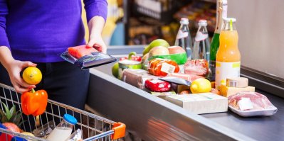 Žena vybaluje u pokladního pásu v supermarketu nákup
