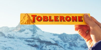 Člověk drží čokoládu Toblerone tak, aby obrázek hory na obalu navazoval na skutečnou horu Matterhorn